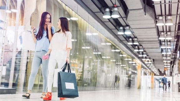 Two women carrying shopping bags and chatting in a mall