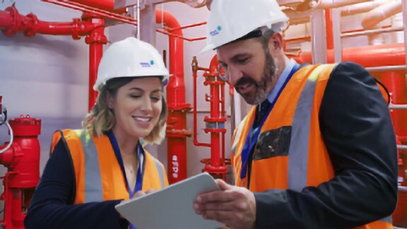 Two colleagues wearing safety equipment in a factory, looking at a tablet