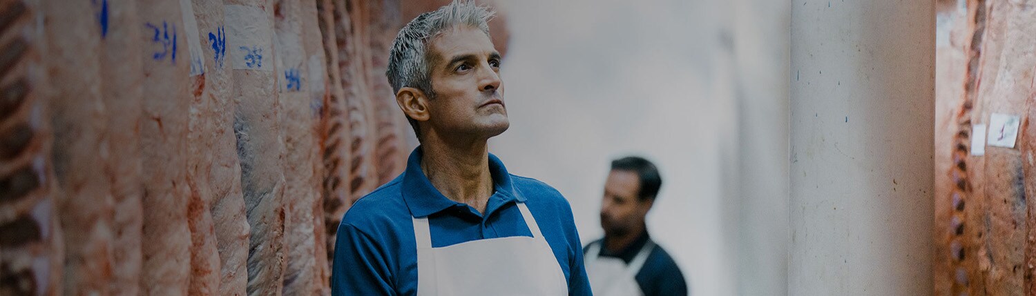 Man in white apron taking stock of processed meat