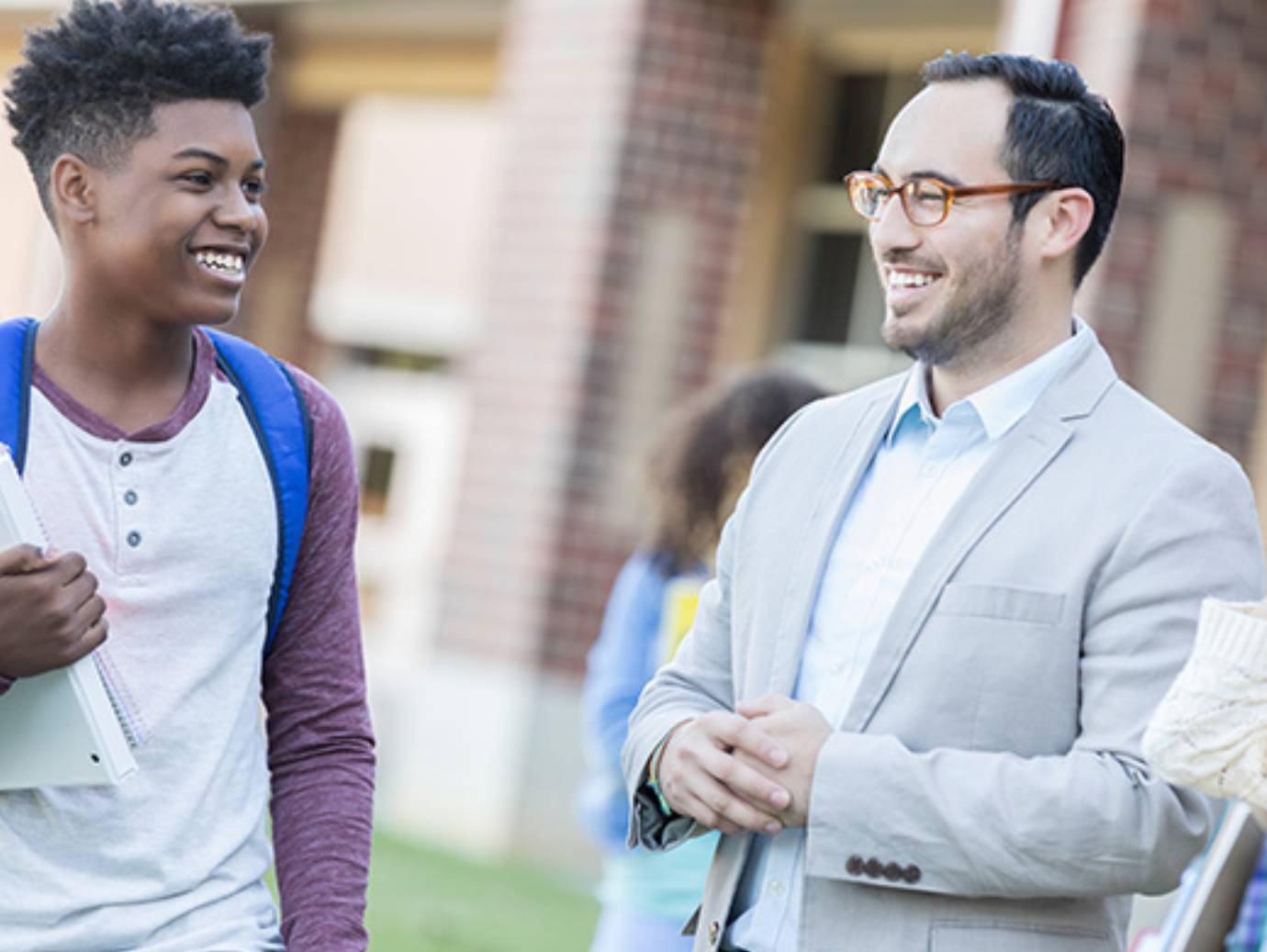 A male student with a backpack smiling and chatting with a professor