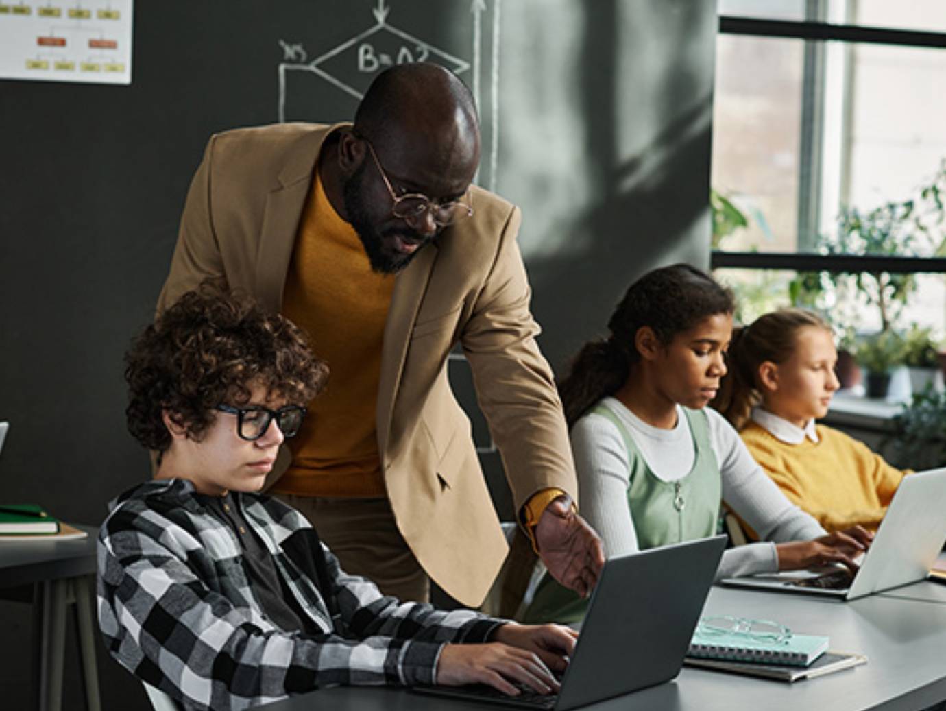 A professor guiding a student using a laptop, in a classroom