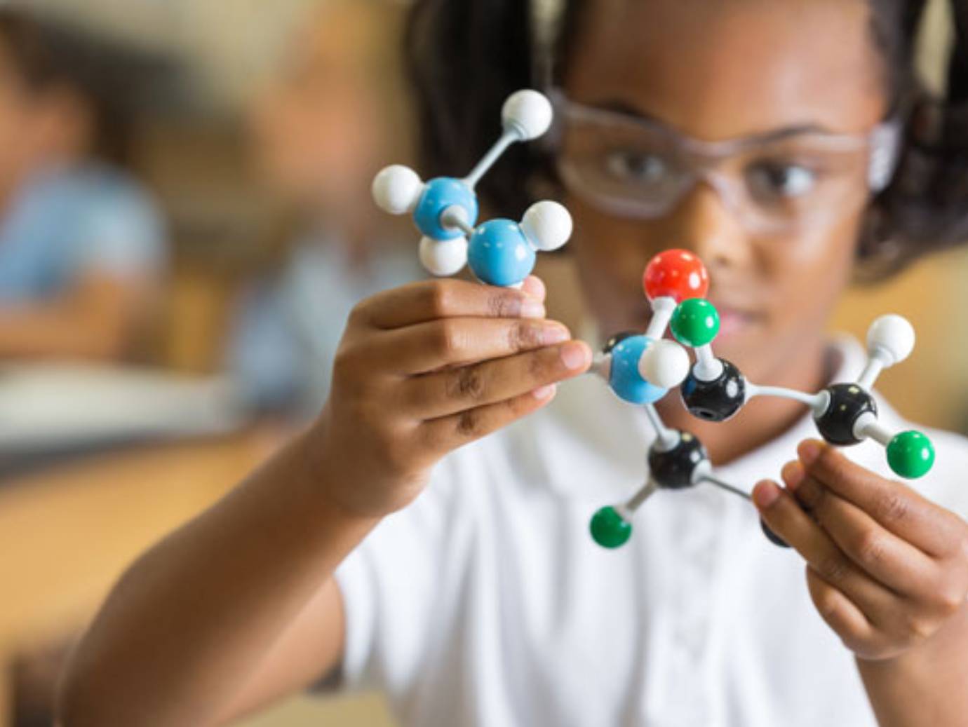 A young girl wearing protective goggles and examining a model of molecules in a science lab
