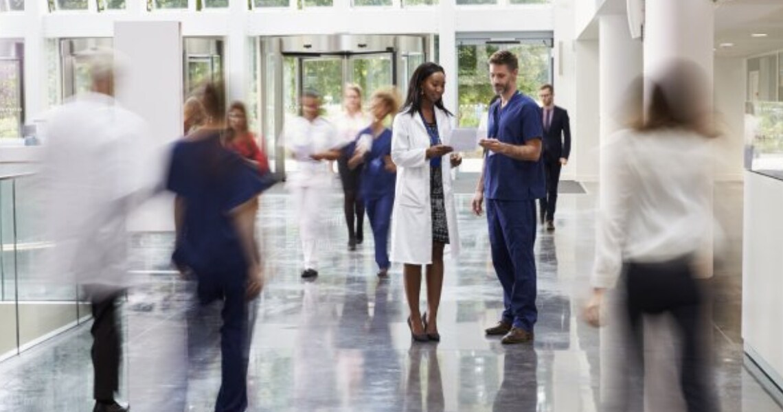 A doctor and a nurse talking in a crowded hospital hallway