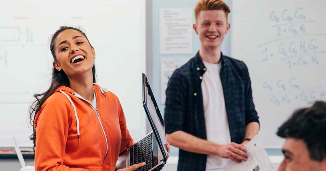 Female student holding a laptop and standing in a classroom