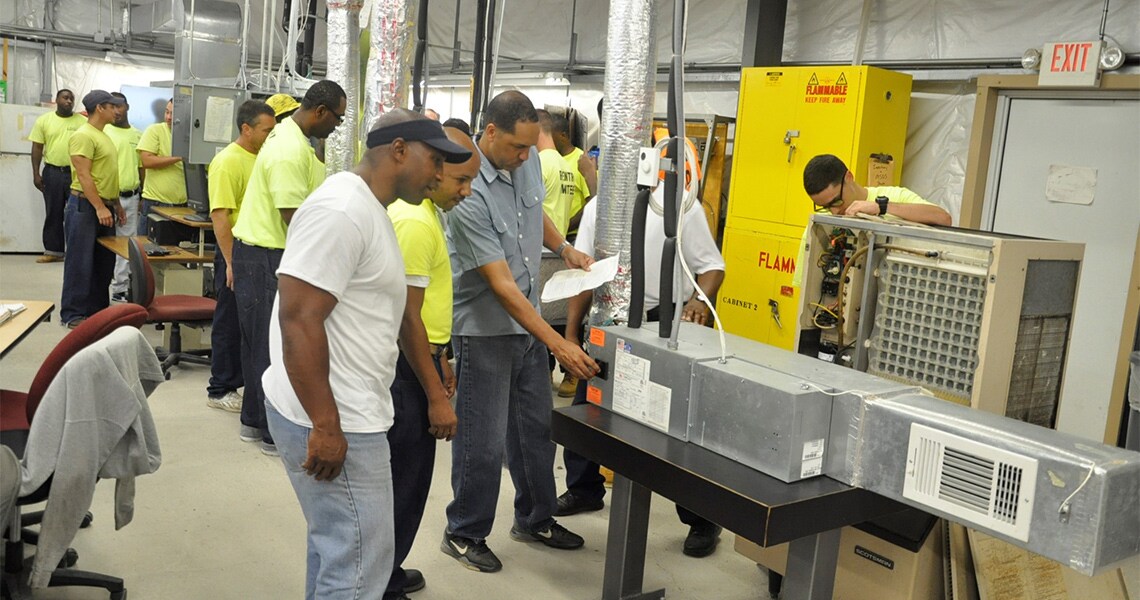 Attendees at an HVAC workshop hosted for former inmates by Johnson Controls, examining HVAC equipment