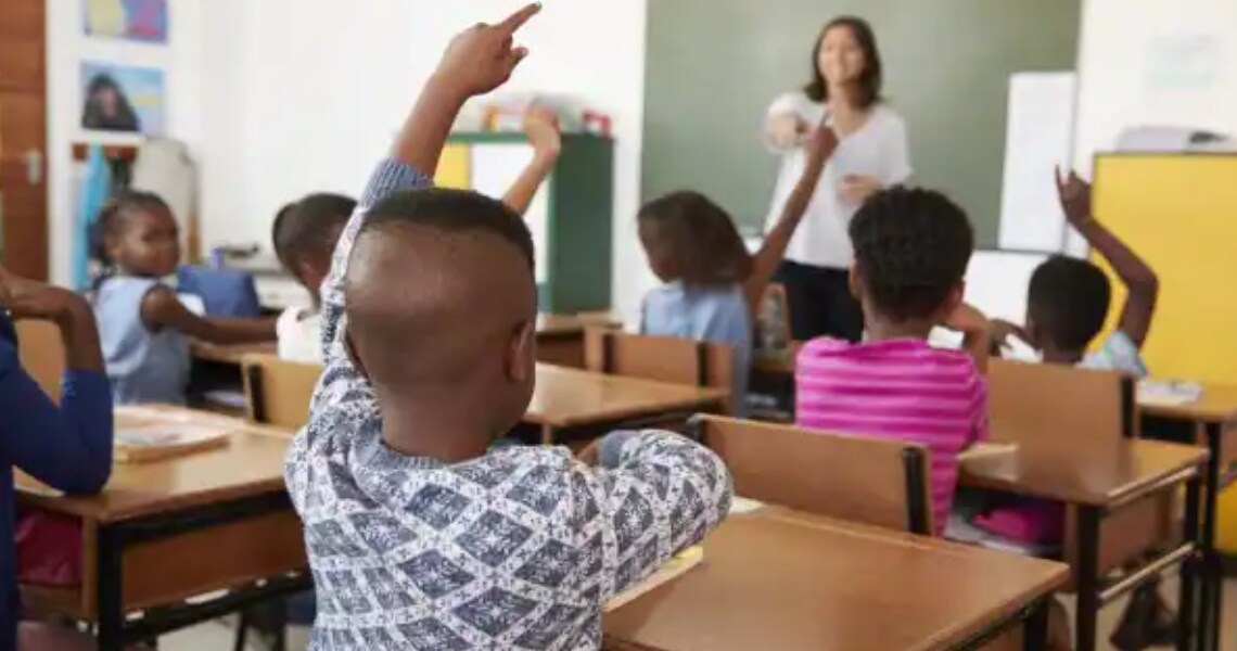 Students raising their hands in a classroom, as the teacher points to one of them