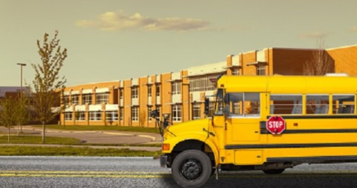 A yellow school bus in front of a school building