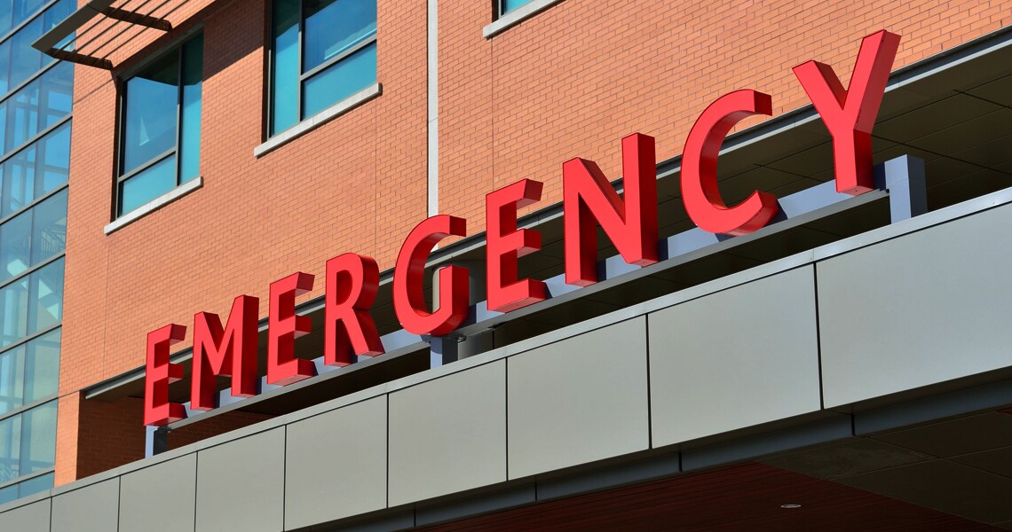 Exterior of a hospital, with a sign displaying 'emergency' in red
