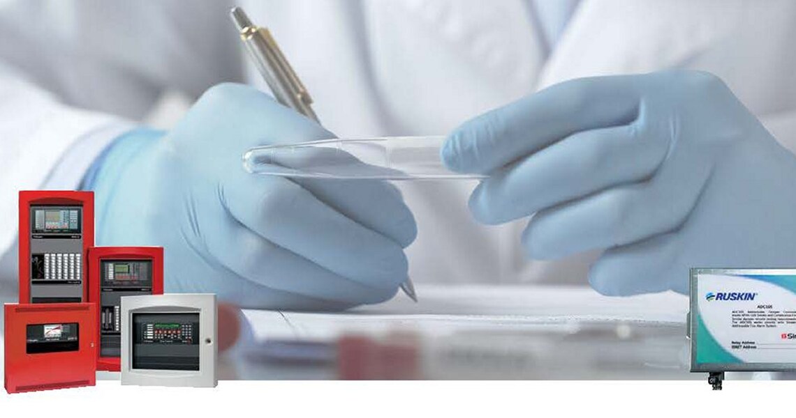 Close-up of a medical professional writing something while holding a glass vial, with Ruskin fire detection units overlaid in the corners