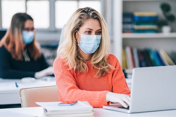 A woman wearing a facemask and scrolling on a laptop