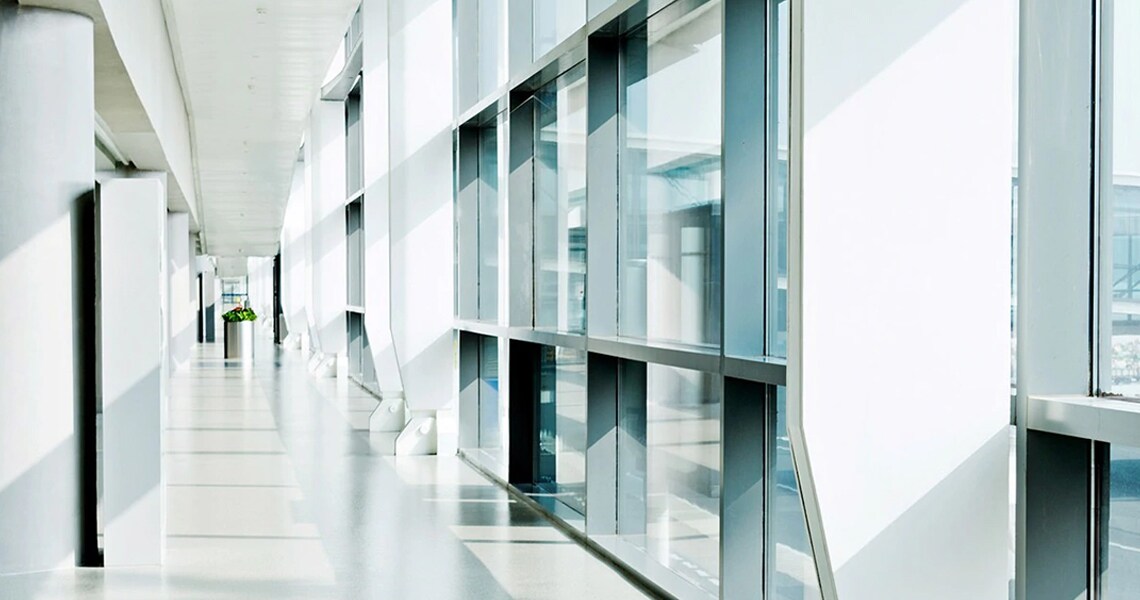 A passage lined with glass windows in a corporate building, with a plant in the far end