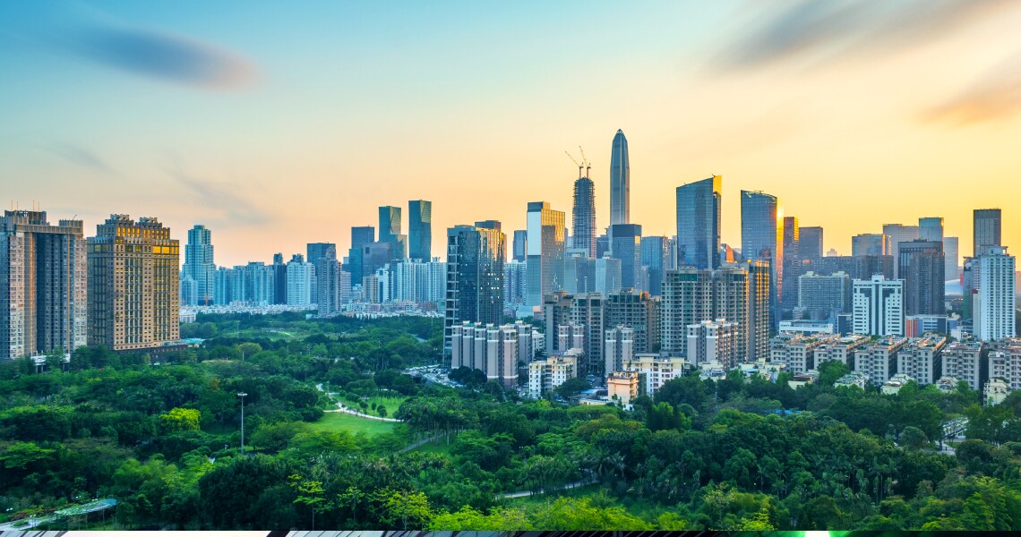 A metropolitan skyline surrounded by greenery, at sunset