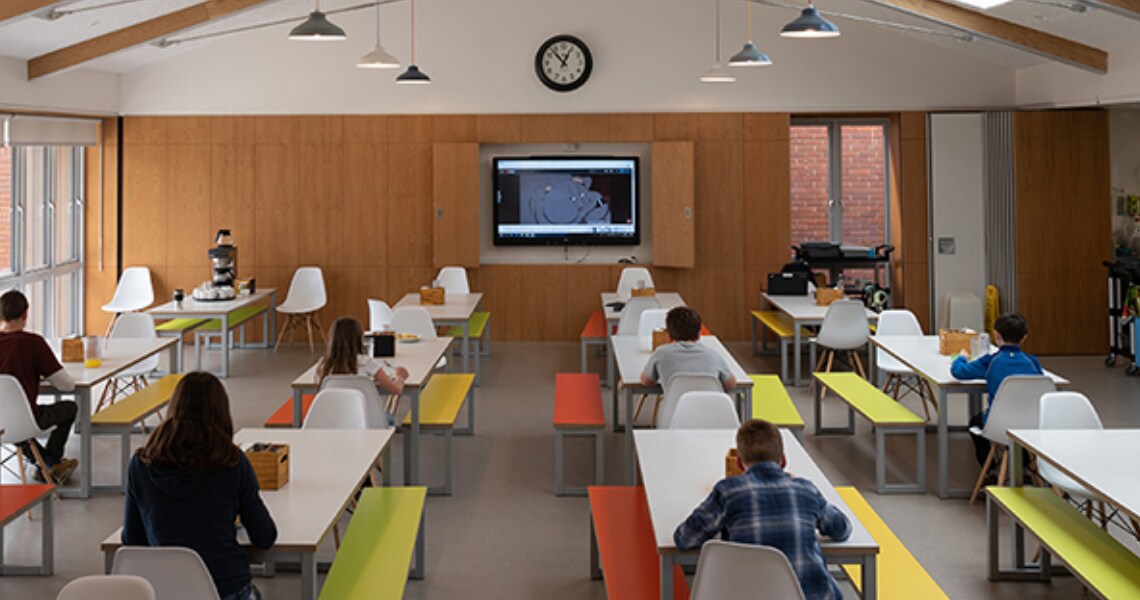 Students seated at a lab and listening to a lecture being played on a screen