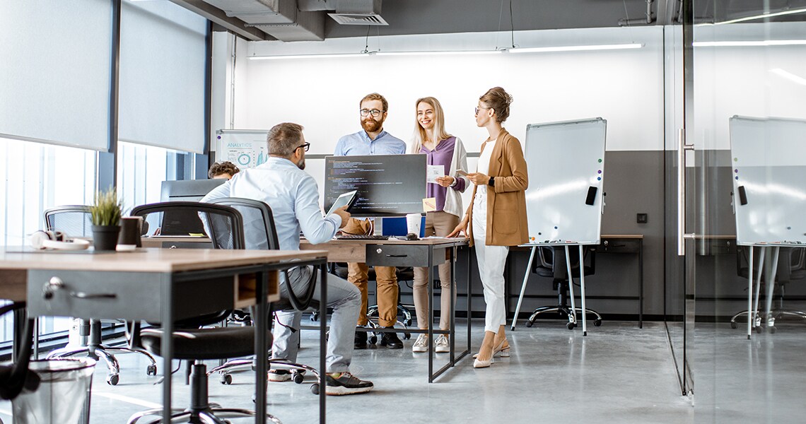 Three colleagues conversing with a man seated on a table in front of them