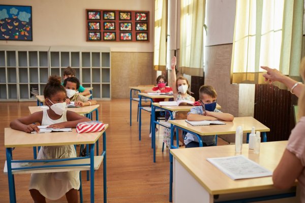 Elementary students in a classroom, with one student with their hand raised