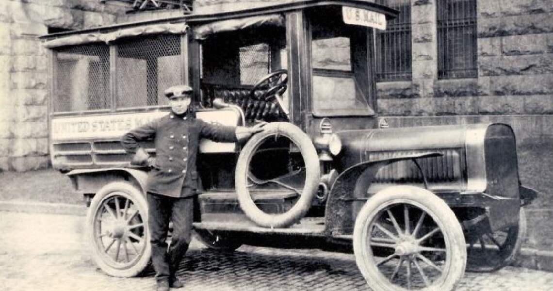 Grayscale image of a man standing near a United States mail truck