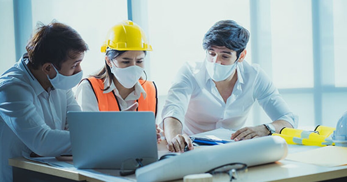 Three technicians with face masks conversing at a conference table