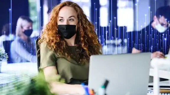 Woman wearing a face mask working in office, overlaid with a graphic of transmission nodes