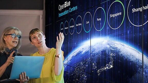 Two female colleagues discussing a presentation on OpenBlue, while one of them holds a laptop