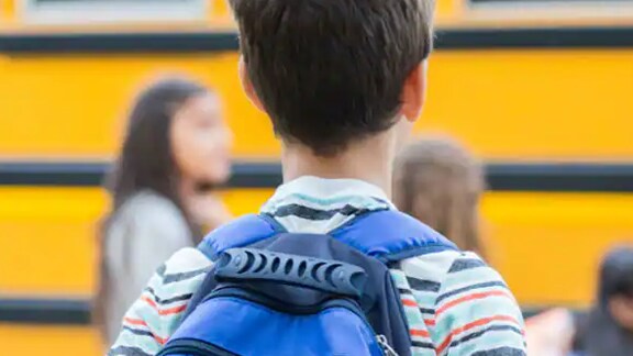 Back view of a kid in front of the school bus