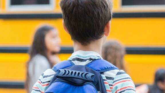 Rear-view of a boy carrying a backpack to school