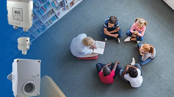 A schoolteacher seated with students on the floor of a library, overlaid with Johnson Controls HVAC products in the left