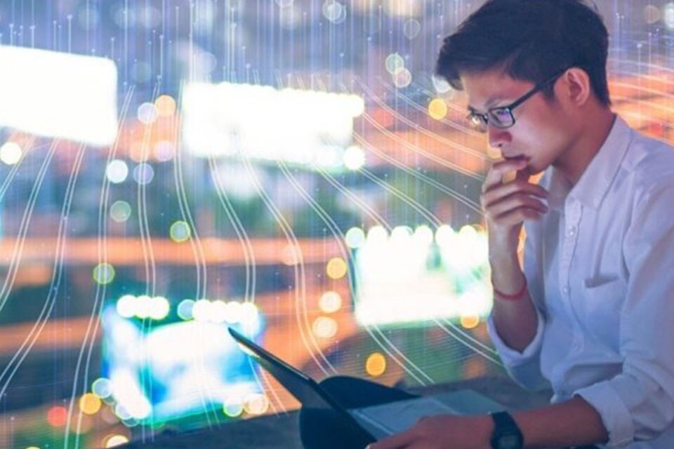 Man wearing glasses and looking at a laptop, with graphics depicting technology in the background