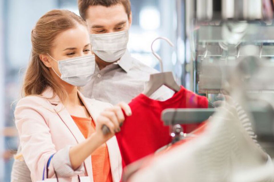 A man and a woman wearing facemarks and picking out clothes from a clothes-rack