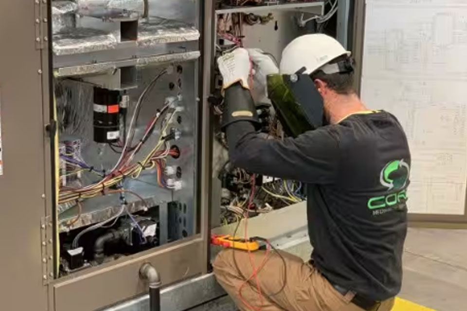 Person in a helmet kneeling and operating HVAC equipment