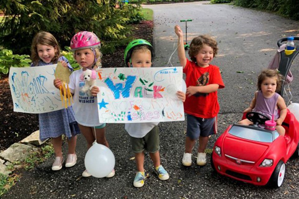 Toddlers wearing bicycle helmets and holding up a sign for the Make-A-Wish walkathon