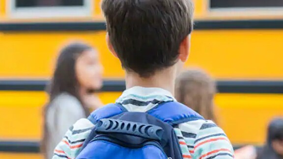 Rear-view image of a boy carrying a backpack to school