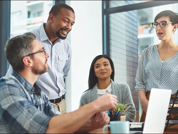 Four colleagues in discussion in front of a laptop on a table