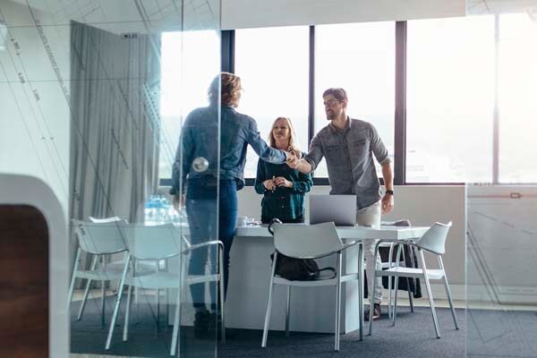 Man and woman smiling and shaking hands with a female client in a conference room