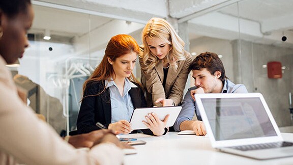 Three employees in discussion at a table, with one holding a tablet