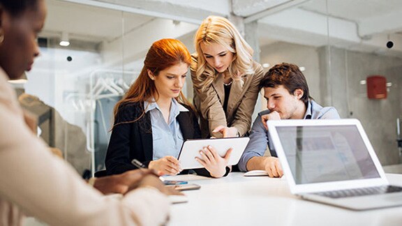 Three employees in discussion at a table, with one holding a tablet